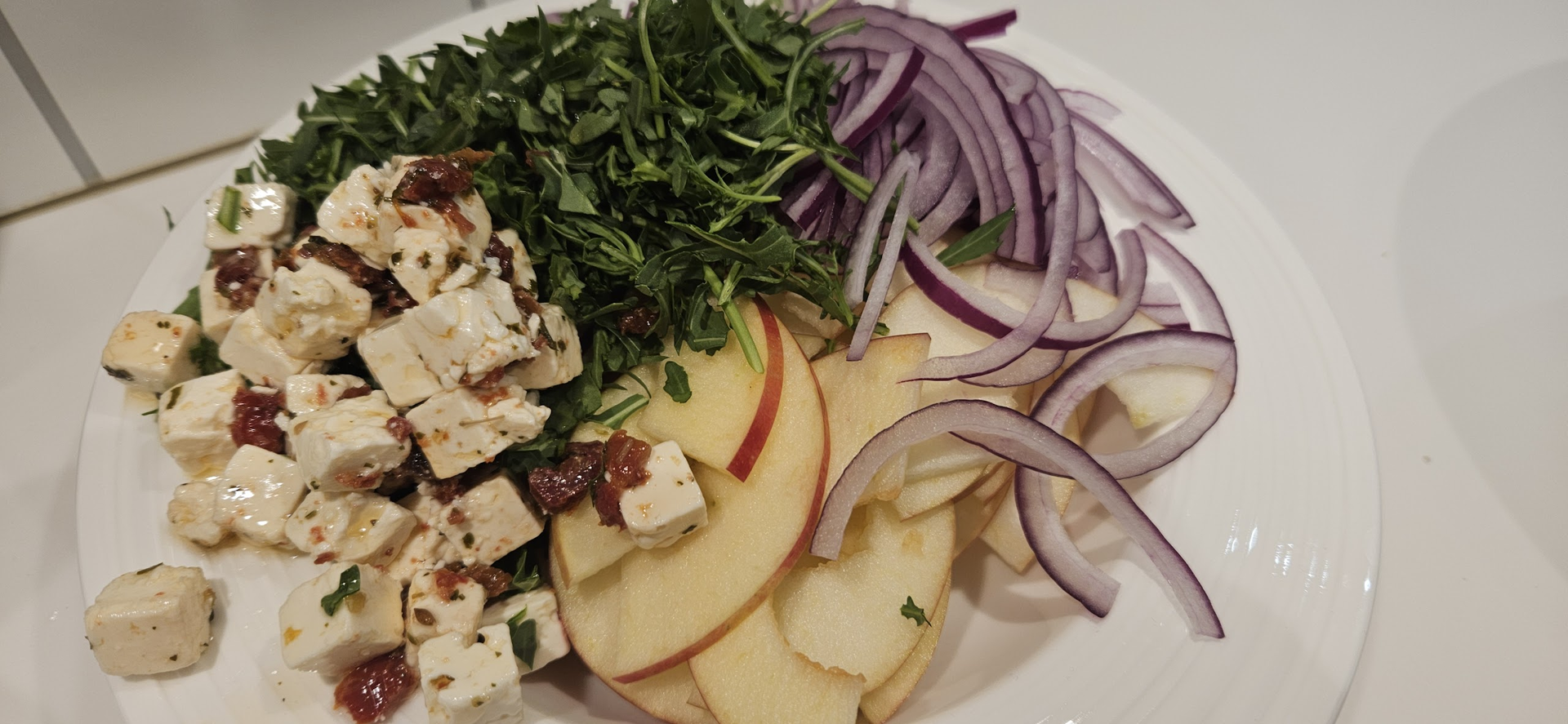 Skjær eple og rødløk tynt, hakk ruccula og vend sammen med feta og Rørosrømme til en skarp eplesalat.